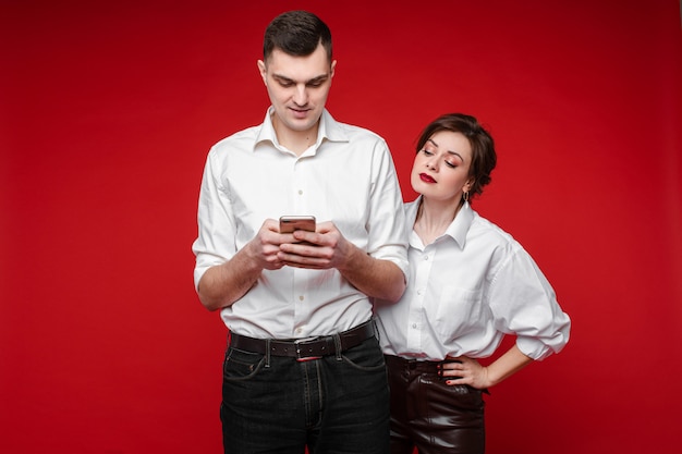 Elle est jalouse de son petit ami et vérifie son téléphone, photo isolée sur le mur rouge