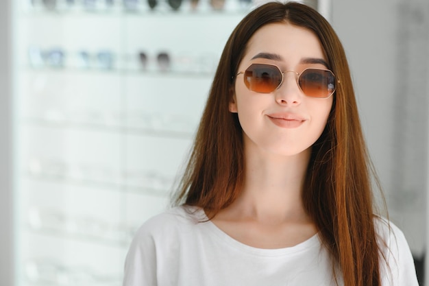 Elle a fait son choix Belle jeune femme ajustant ses nouvelles lunettes de soleil et souriant tout en se tenant dans un magasin d'optique