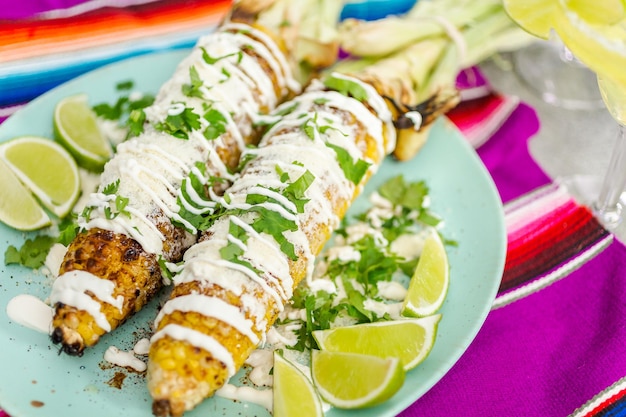 Elote de maïs de rue mexicaine grillée garnie d'épices et de coriandre fraîche sur une assiette de service.