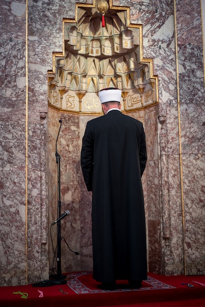 Photo emam dans la mosquée avec des vers de kuran sur le mur