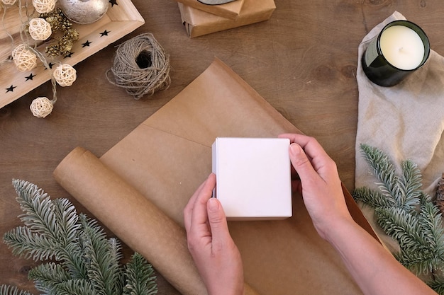 Emballage cadeau personne tenant une boîte présente sur le lieu de travail avec du papier kraft sur une table en bois