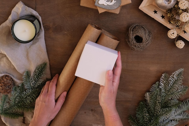 Emballage cadeau personne tenant une boîte présente sur le lieu de travail avec du papier kraft sur une table en bois