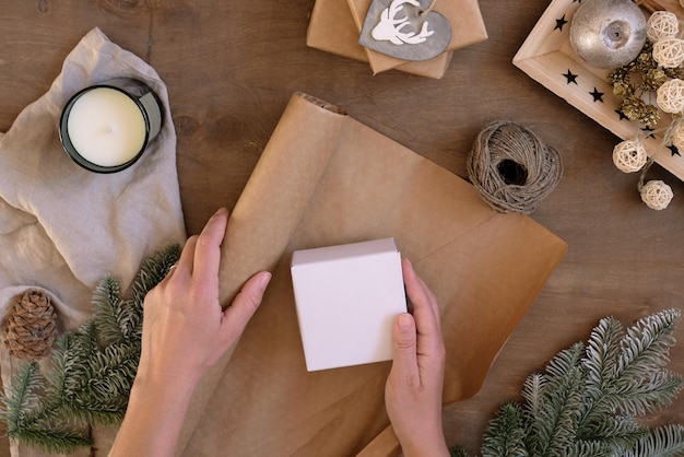 Emballage cadeau personne tenant une boîte présente sur le lieu de travail avec du papier kraft sur une table en bois