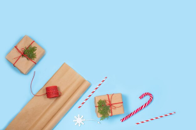 Emballage des cadeaux de Noël dans du papier kraft avec des accessoires écologiques Branches d'arbres de Noël, coffrets cadeaux et cordes sur une table bleue.