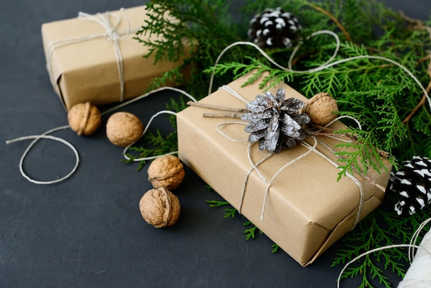 Emballage de cadeaux de Noël écologiques avec du papier kraft, des ficelles et des branches de sapin naturel sur fond sombre
