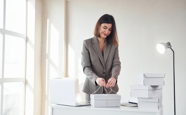 Emballage des commandes dans les boîtes blanches Jeune femme en vêtements formels est à l'intérieur Conception du style