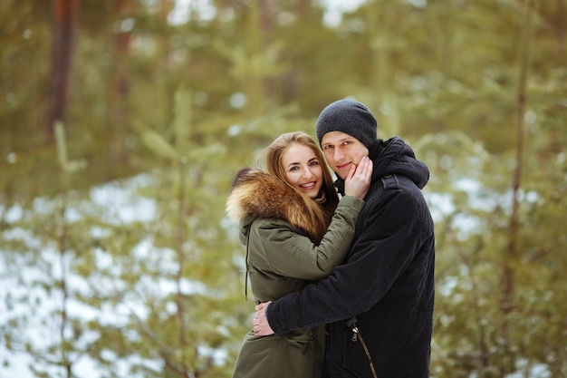 Embrassant le couple regardant la caméra avec des sourires dans le parc d'hiver