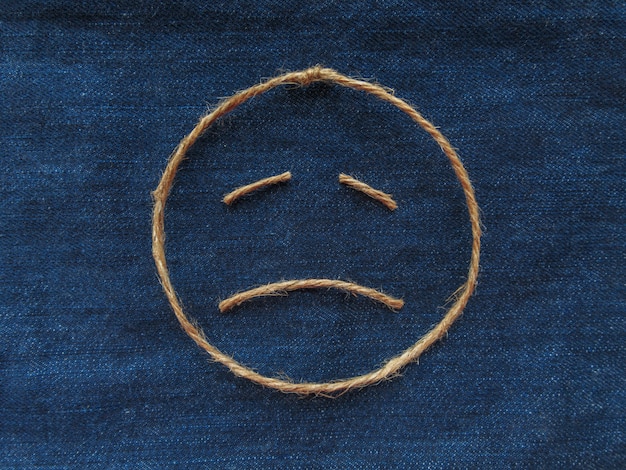 Photo emoji. smiley triste en ficelle sur denim bleu. fermer