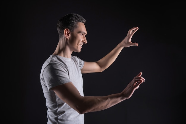 Des émotions agréables. Smart bel homme gai souriant et regardant l'écran virtuel tout en profitant de la technologie moderne