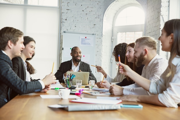 Émotions heureuses. Groupe de jeunes professionnels ayant une réunion. Un groupe diversifié de collègues discute de nouvelles décisions, plans, résultats, stratégie. Créativité, lieu de travail, affaires, finance, travail d'équipe.
