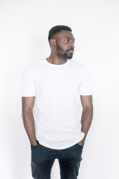 Émotions humaines positives, expressions faciales, sentiments, attitude et réaction. Sympathique jeune homme afro-américain vêtu d'un t-shirt blanc et d'un jean posant en studio sur fond blanc
