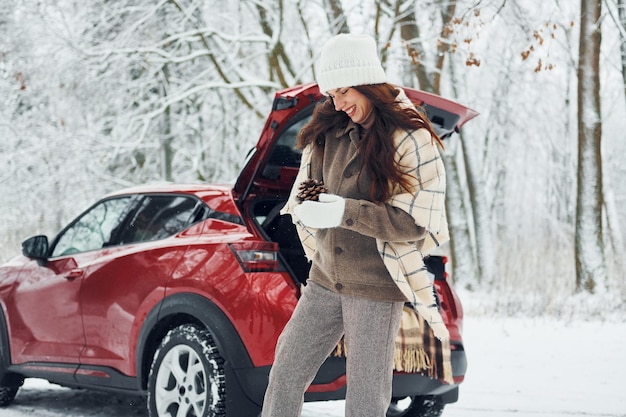 Photo Émotions joyeuses belle jeune femme est à l'extérieur près de son automobile rouge à l'heure d'hiver