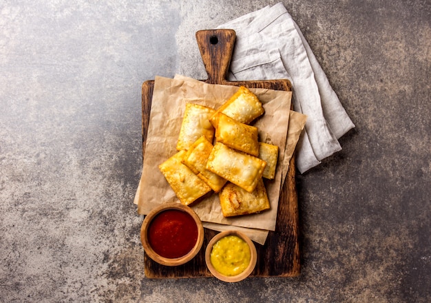 Empanadas au fromage frit. Snack traditionnel d&#39;Amérique latine servi sur une planche en bois avec sauce chili et moutarde.