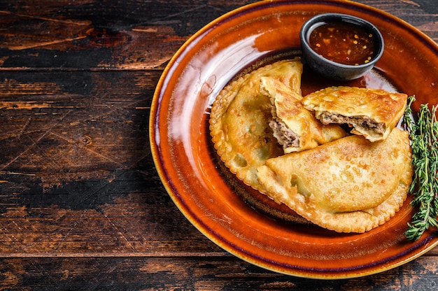 Empanadas frites avec de la viande de boeuf hachée servies sur une assiette avec une sauce chili. Fond en bois sombre. Vue de dessus. Espace de copie.