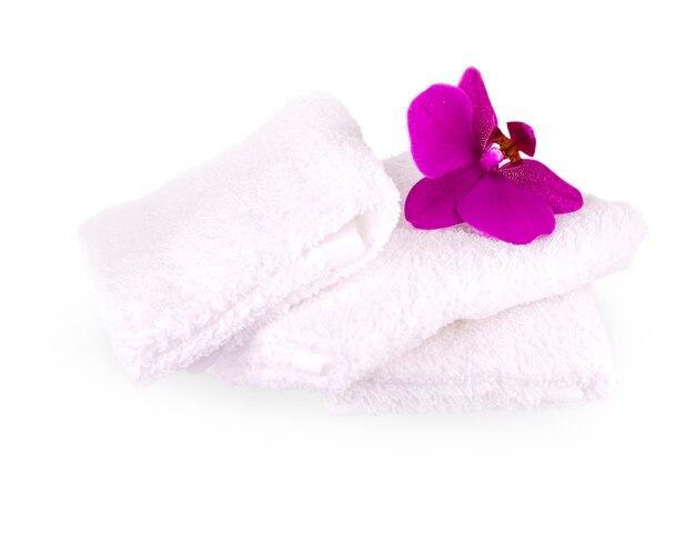Empilez des serviettes de spa blanches sur fond blanc avec une fleur d'orchidée violette.
