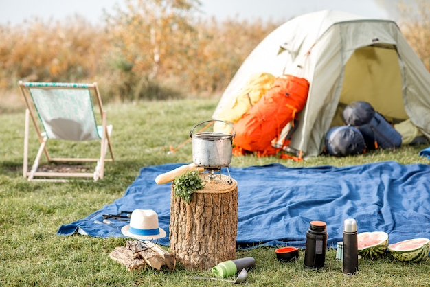 Emplacement de camping avec tente, sacs à dos, chaise et équipement de randonnée à l'extérieur sur la pelouse verte