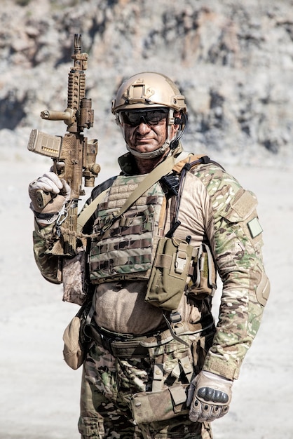 Emplacement demi-longueur portrait de gros soldat musclé en uniformes de terrain avec fusil dans le désert parmi les rochers