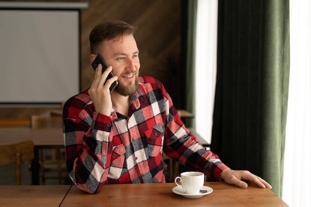 Employé américain riant appelant ses amis pendant les heures de travail et buvant du café au bureau téléphones portables au travail