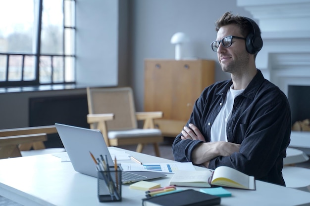 Employé de banque allemand positif assis sur le lieu de travail au bureau à domicile moderne dans des écouteurs sans fil