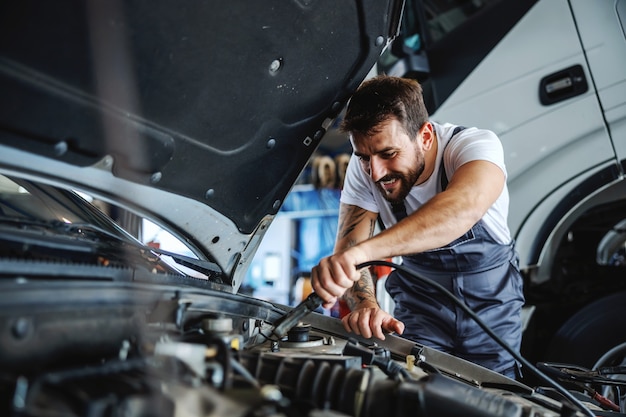 Employé barbu dévoué et travailleur en salopette fixant le moteur. Concept de travaux manuels.