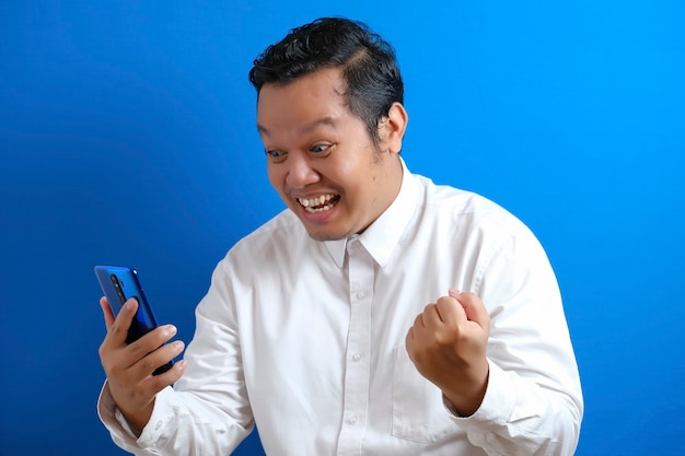 Un employé de bureau asiatique a l'air confiant tout en accédant à son téléphone intelligent, l'homme montre une expression surprise