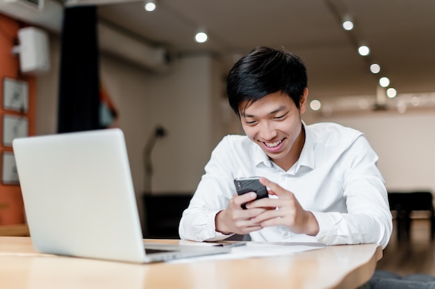 Employé de bureau asiatique souriant utilise un téléphone et un ordinateur portable