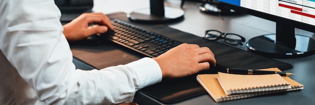 Employé de bureau assis sur le bureau de l'espace de travail concentré et engagé à l'aide d'un ordinateur et en tapant sur le clavier pour saisir des données afin d'assurer une gestion précise des données dans le lieu de travail moderne