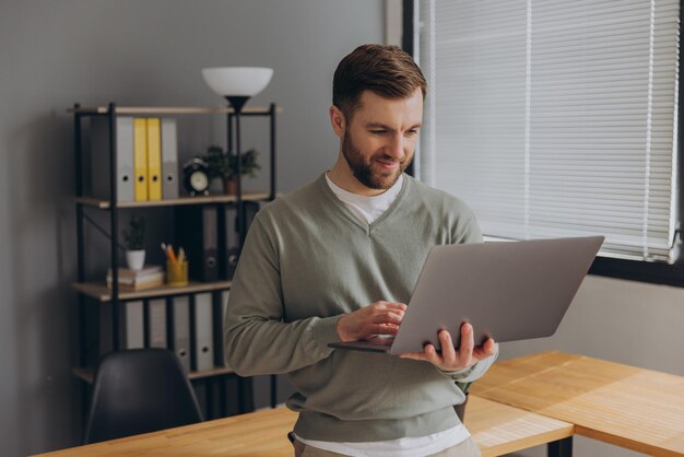 Un employé de bureau à barbe heureux et moderne d'une entreprise informatique souriant et tenant un ordinateur portable au bureau