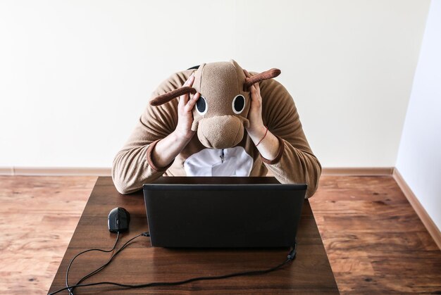 Employé de bureau en costume cosplay d'une vache. Guy dans les vêtements de nuit pyjama animaux drôles près de l'ordinateur portable. Parodie sur un manager désespéré. L'épuisement professionnel.