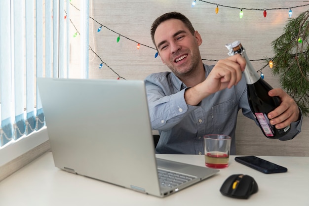 L'employé de bureau fête Noël au travail. Fêter Noël et le Nouvel An sur le lieu de travail. Un employé de bureau boit de l'alcool. Communication à distance. célébrer la nouvelle année à distance