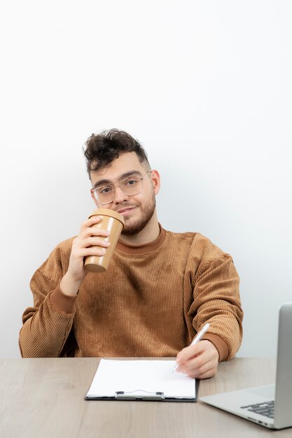 Employé de bureau masculin assis au bureau avec une tasse de café et prendre des notes.