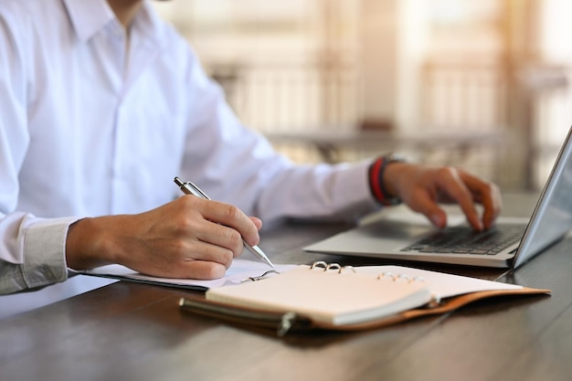 Employé de bureau masculin utilisant un ordinateur portable et écrivant des informations sur un ordinateur portable