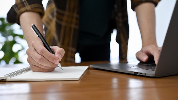 Un employé de bureau professionnel en chemise de flanelle travaillant à son bureau en prenant des notes et en utilisant un ordinateur portable