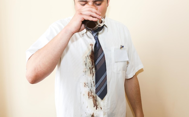 Un employé de bureau renverse du café sur une chemise blanche. L'épuisement professionnel. Gestionnaire malheureux avec une tasse dans les mains. Travail stressant. Homme désespéré.