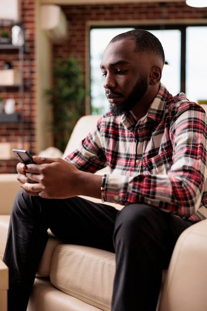 Employé de bureau surfant sur l'application de médias sociaux sur téléphone mobile, naviguant sur le site Internet et faisant un travail indépendant à distance. Homme utilisant le web en ligne sur smartphone, assis sur un canapé et travaillant à domicile.