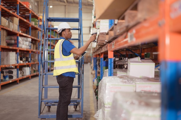 Un employé de bureau utilise une tablette numérique alors qu'il se tient sur les escaliers d'un entrepôt pour inspecter les marchandises.