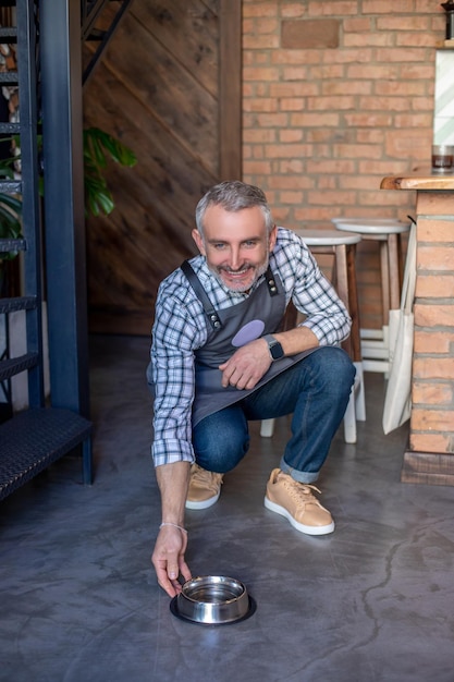 Employé de café souriant dans le tablier mettant un bol de chien en acier inoxydable sur le sol