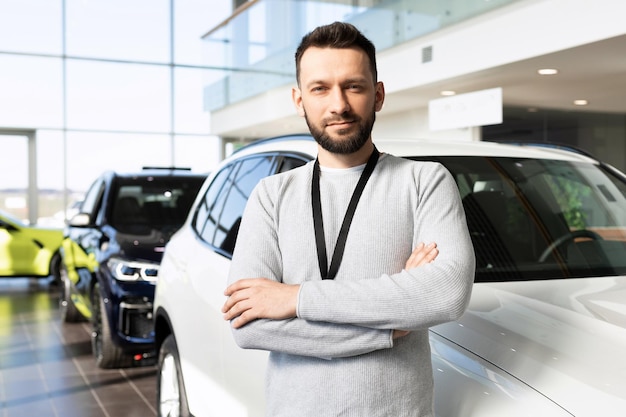 Employé d'un concessionnaire automobile à côté d'une nouvelle voiture regardant la caméra avec un sourire