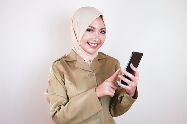 Un employé du gouvernement souriant montrant un écran vide sur un smartphone Un jeune PNS musulman asiatique portant l'uniforme kaki et le hijab