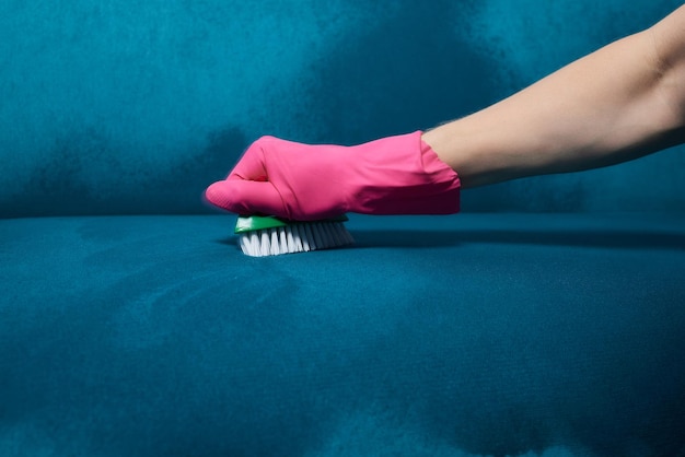 L'employé du nettoyeur à sec main dans des gants de protection enlevant la tache du canapé gris avec une brosse et un spécial