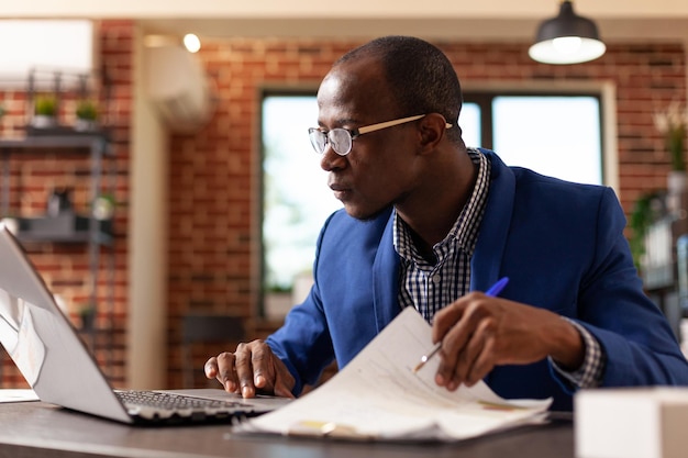 Employé de l'entreprise analysant des documents sur le presse-papiers pour planifier une stratégie commerciale avec un ordinateur portable. Entrepreneur utilisant des documents informatiques et financiers pour travailler sur un projet marketing. Personne concentrée