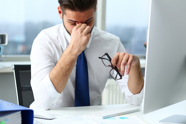 Employé fatigué à l'ordinateur portable pc lieu de travail portant des lunettes