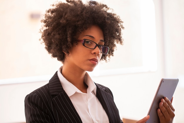 Employé de femme d'affaires dans des verres travaillant au bureau avec tablette regardant la caméra