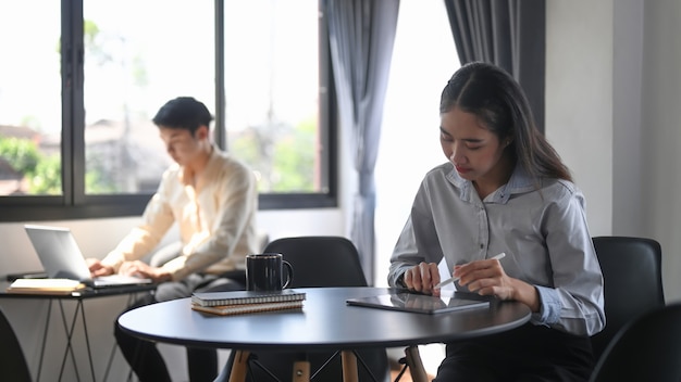 Employé de femme travaillant avec une tablette numérique alors qu'il était assis avec son collègue dans la salle de bureau.