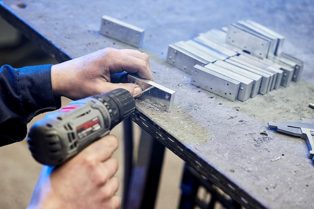 Employé forant une plaque d'acier plate en aluminium avec une perceuse d'établi Le foret en métal fait des trous dans la billette d'acier sur une machine industrielle Industrie du travail du métal Gros plan