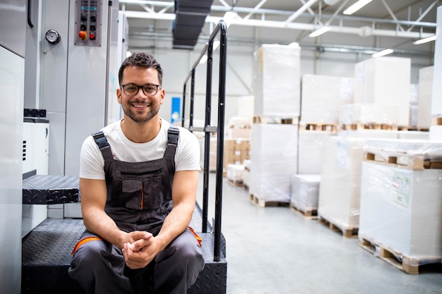 Employé D'impression Assis Près De La Machine D'impression Avec De Grandes Piles De Feuilles En Arrière-plan