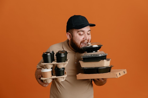 Employé de livreur en casquette noire et uniforme de t-shirt blanc tenant des tasses à café et des récipients alimentaires heureux et joyeux s'amusant debout sur fond orange