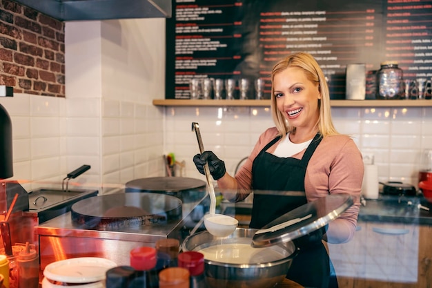 Un employé de magasin de crêpes heureux tient une louche avec un mélange de crêpes et sourit à la caméra