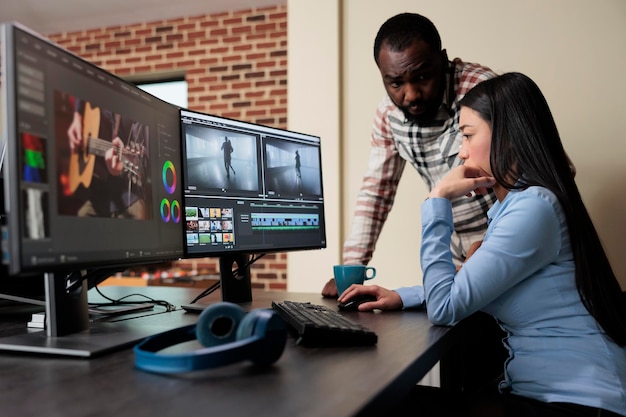 Employé de la maison de post-production discutant avec un collègue de la qualité des images. Monteur de film professionnel assis au bureau tout en améliorant les images de film à l'aide d'un logiciel spécialisé avancé.