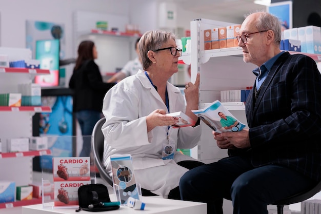 Employé de la pharmacie expliquant au patient les instructions de dosage des suppléments cardiaques. Homme âgé écoutant un assistant en pharmacie parler des bienfaits des vitamines et des effets secondaires chez l'apothicaire